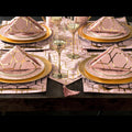 A table setting with pink and gold geometric patterned placemats and a runner, including matching square napkins.