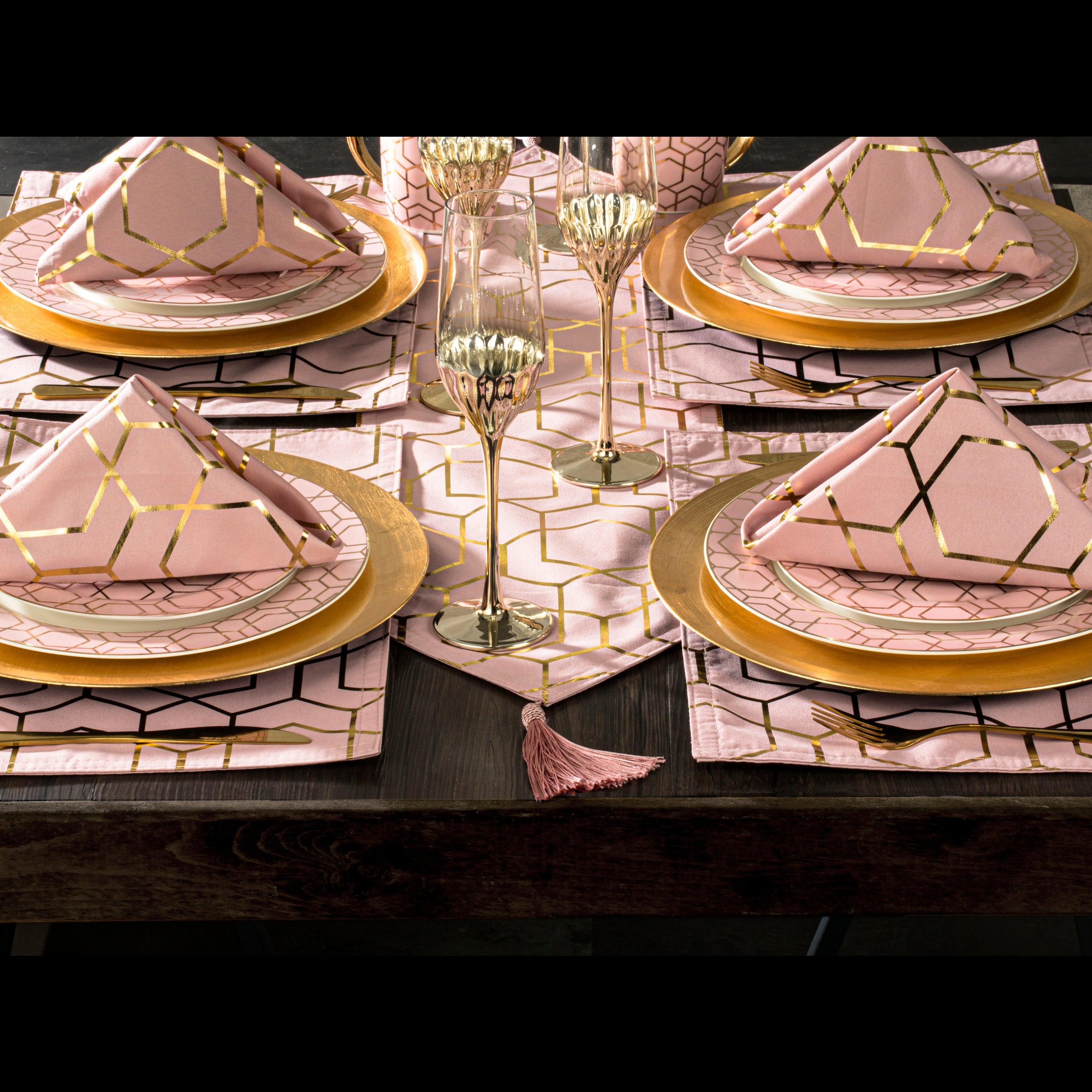 A table setting with pink and gold geometric patterned placemats and a runner, including matching square napkins.