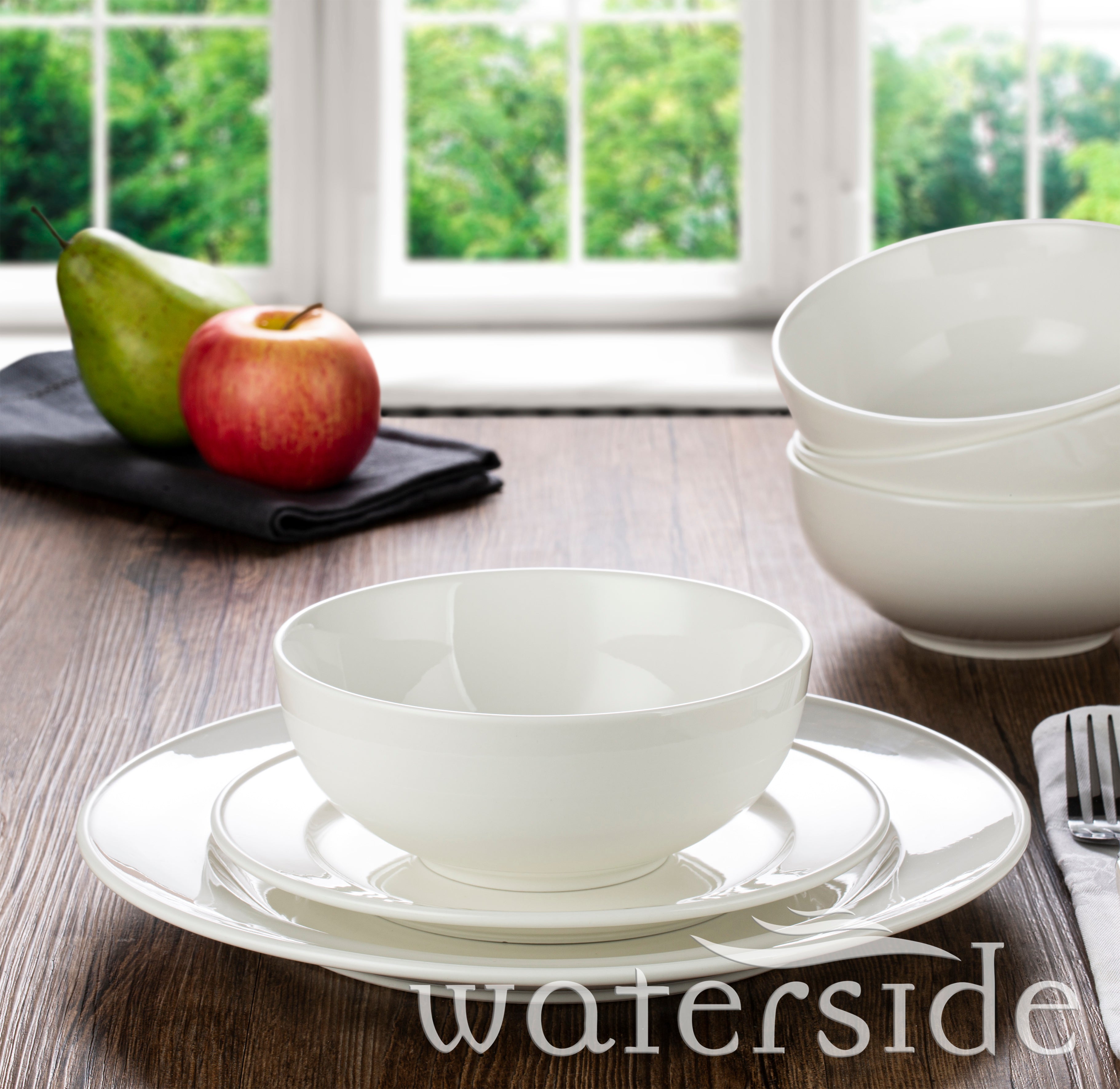 White ceramic bowls and plates on a wooden table with a view of greenery outside.