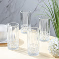 Set of four clear glass tumblers on a marble surface with a plant and flowers in the background.