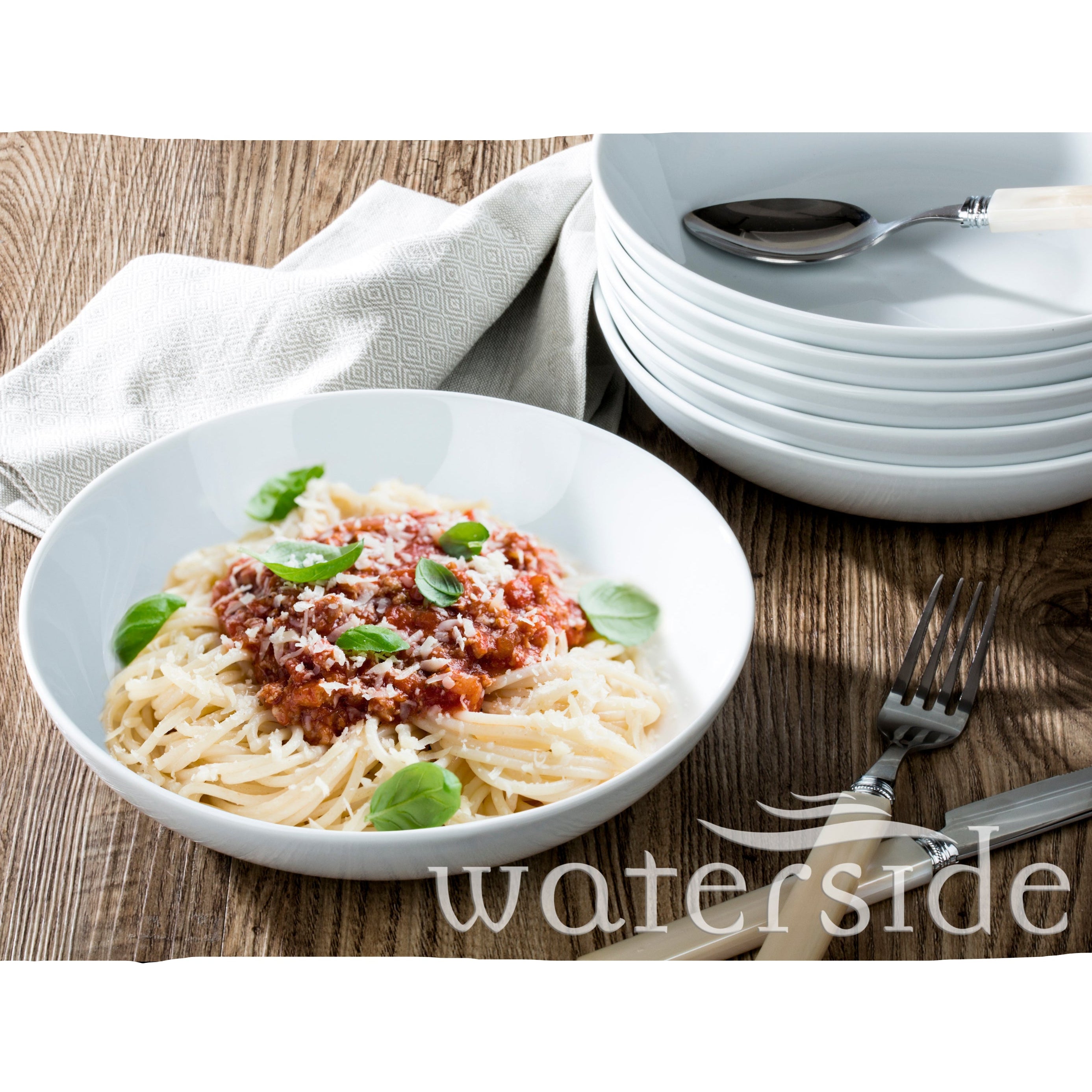 Pasta dish with tomato sauce and basil leaves in a white bowl on a wooden table, with 'waterside' branding.